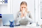 A woman sneezes while sitting at her desk.