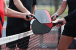 Pickleball players hold together their rackets over the net on a pickleball court.