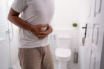 A man holding his stomach in pain in front of toilet.