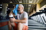 A older man wiping sweat from his head at gym after exercise.