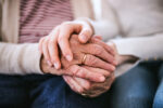 A person holding the hand of an aging loved one.