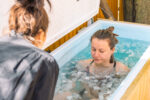 Woman doing cold water therapy in a tub as a friend cheers her on.