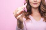 Woman in pink sweater with pink ribbon supporting breast cancer awareness campaign. Breast Cancer Awareness