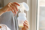 A woman holding up a breastfeeding pump with breast milk inside baby bottle.