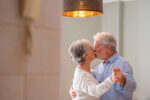 Senior couple kisses as they dance in their home.