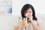 A woman who is sick with a cold holding a glass of orange juice.