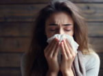 A woman is congested and blowing her nose is a tissue.