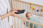 Parent looking at phone for advice while overlooking their child in a crib.