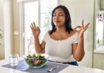 A young woman practicing mindfulness through meditation next to healthy food.