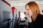 A woman experiencing jet lag yawns on a plane.
