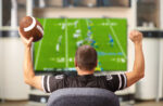 A man cheering on a football team on television screen that he has been gambling on.