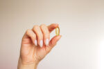 A woman's hand holding a fish oil supplement.