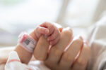 A premature NICU baby holds parent's finger.