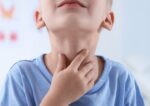 A child holding the outside of his neck where his thyroid glands are.