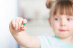 A child holding up a medication that is not hers.