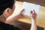 A woman looking at the calendar to see how she can plan her period to avoid a certain upcoming event.
