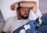 A man sick with a cold sleeps in his bed to recover faster from sickness.
