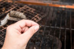 A person holding up a wire grill brush bristle over a grill.